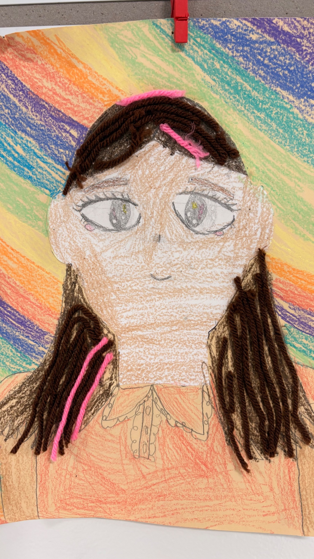 Mixed-media self portrait with brown yarn pigtails on a rainbow background