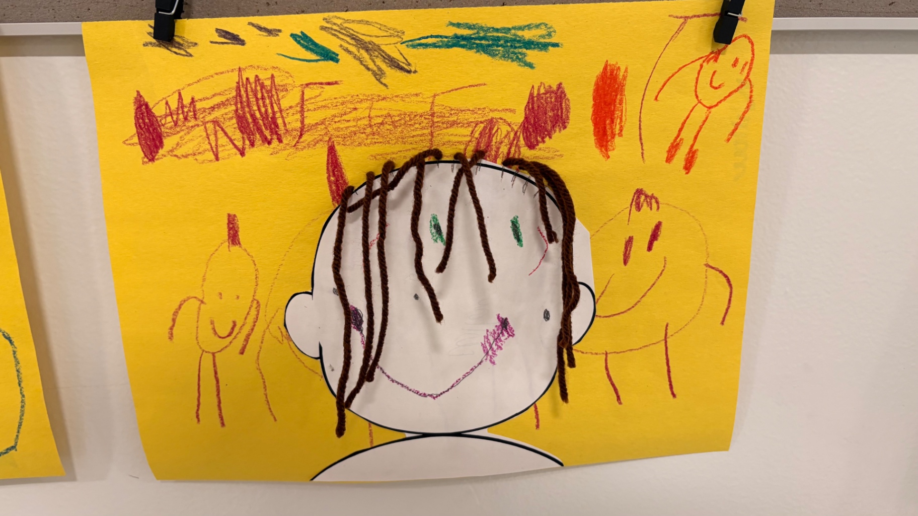 Self portrait with brown yarn hair surrounded by crayon family drawings