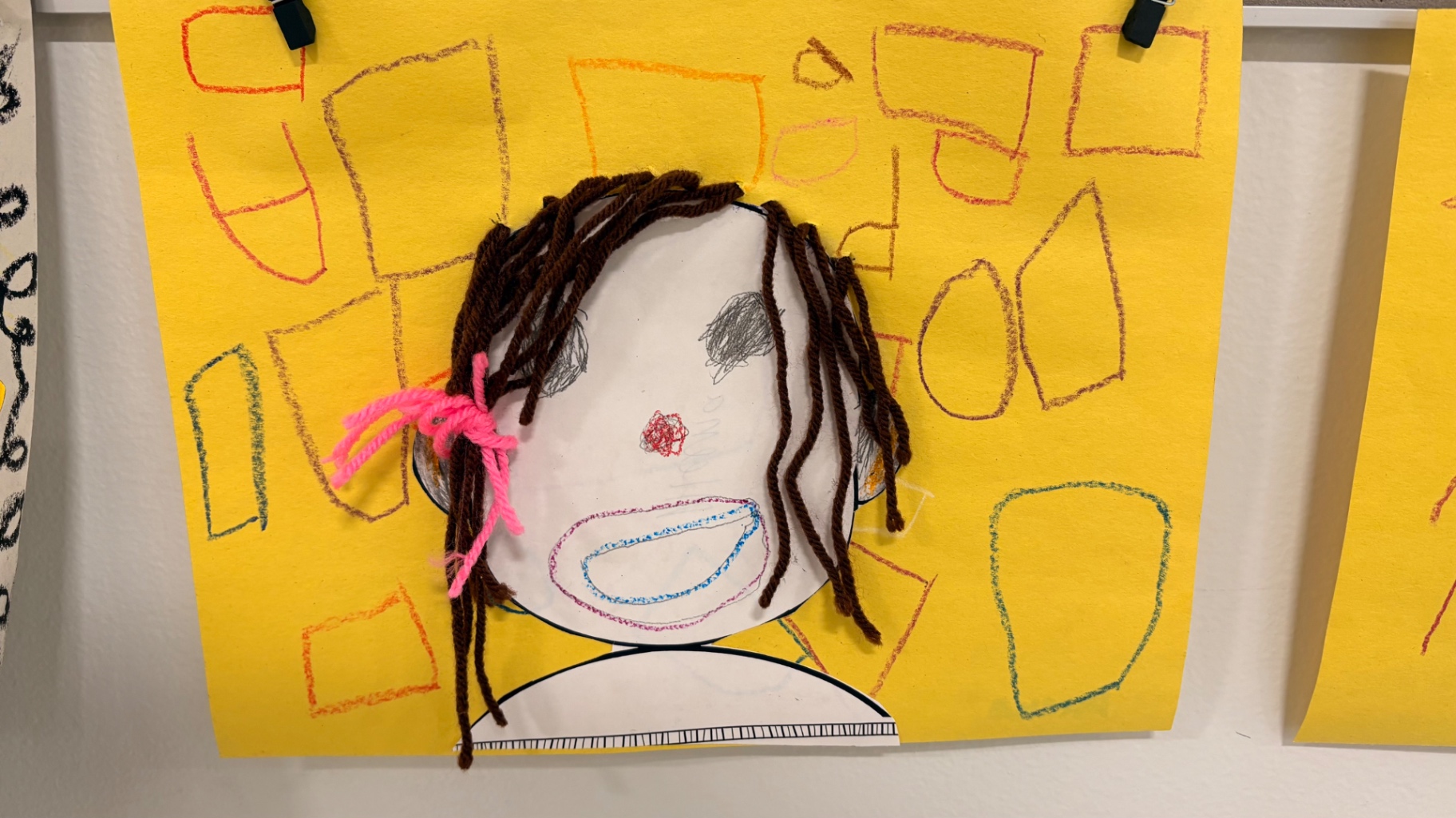 Self portrait with brown yarn hair and pink ribbon on yellow paper